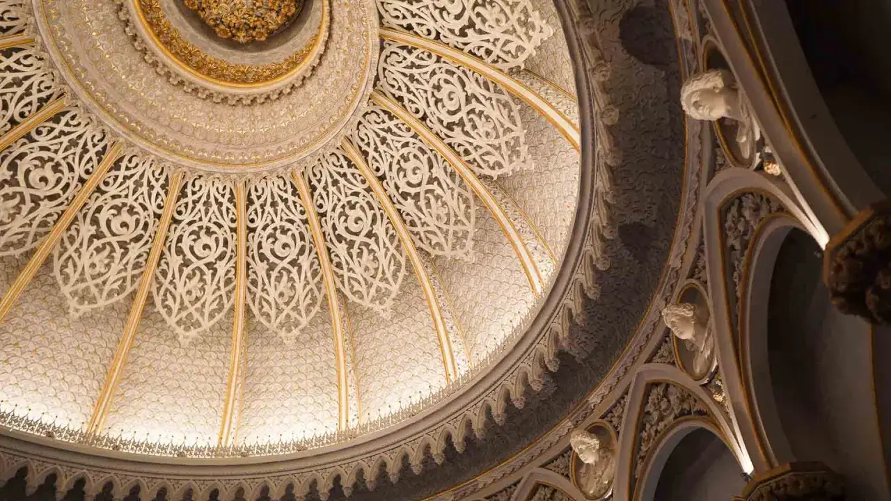 Intricate dome of Monserrate Palace, featuring ornate white lacework, gold accents, and sculpted busts.