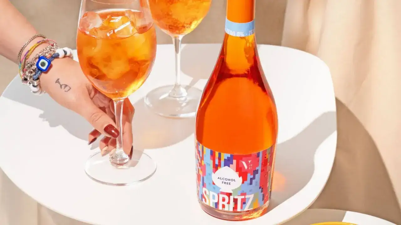 Orzeźwiający aperol bezalkoholowy w szklance z lodem i butelka na stole. Idealny na letnie popołudnie.