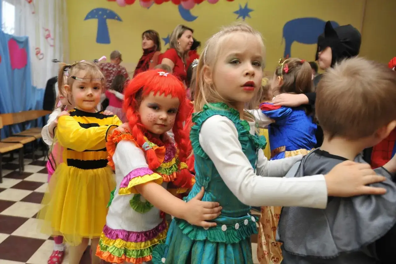 Dzieci w barwnych strojach, pszczółka, klaun i księżniczka, bawią się na balu karnawałowym.