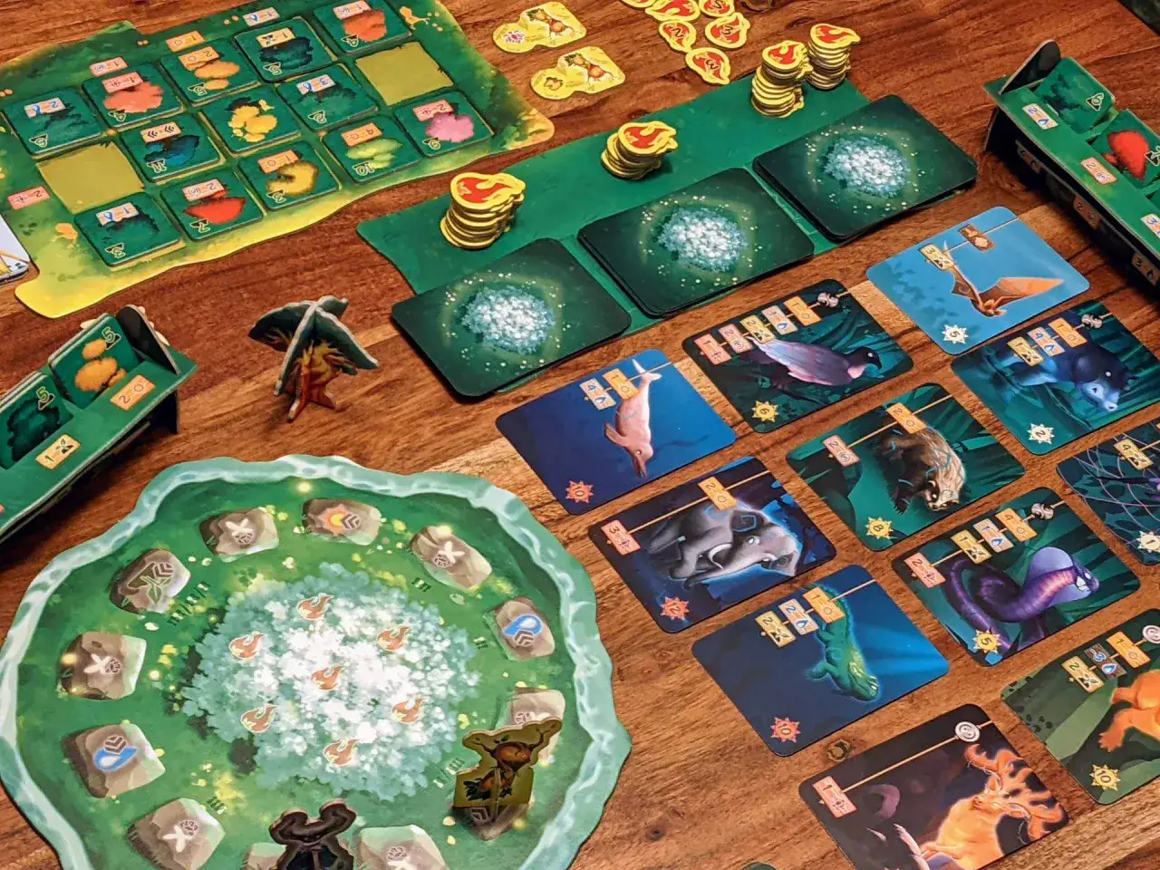 Brettspiel-Komponenten f&uuml;r ein Kennerspiel: bunte Tierkarten, Spielbrett mit Symbolen, Holzfiguren und Marker.