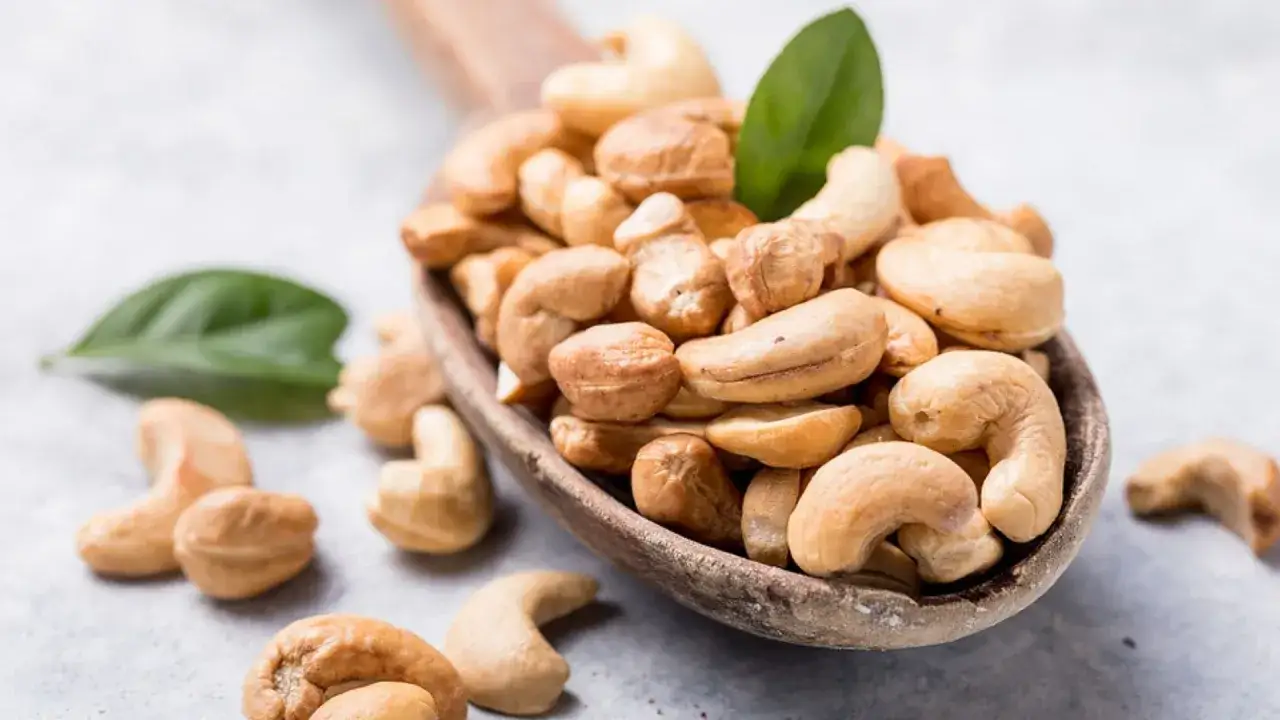 Holzschale voller Cashewkerne, ideal für die Schwangerschaft. Zwei grüne Blätter liegen daneben.