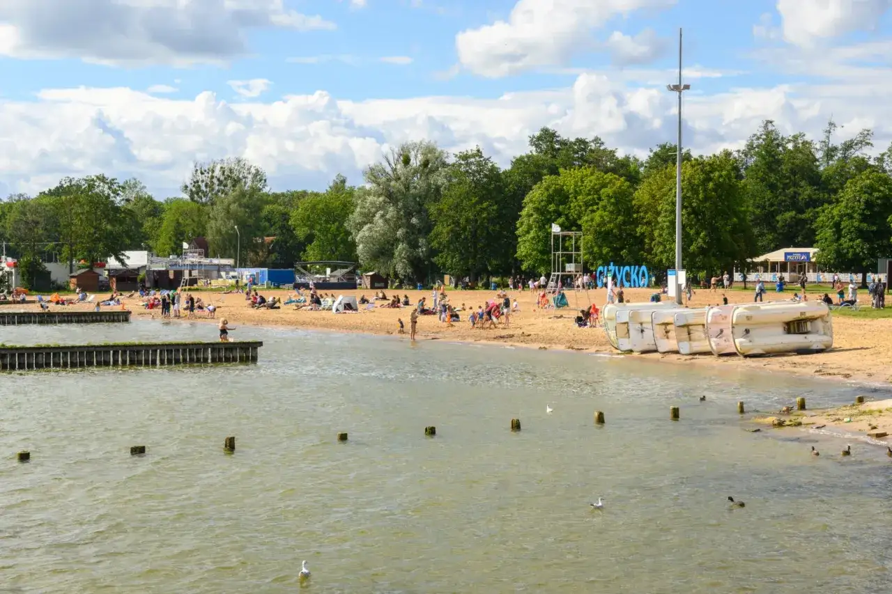 Słoneczny dzień na plaży na Mazurach z dziećmi. Ludzie odpoczywają, bawią się i kąpią w jeziorze.