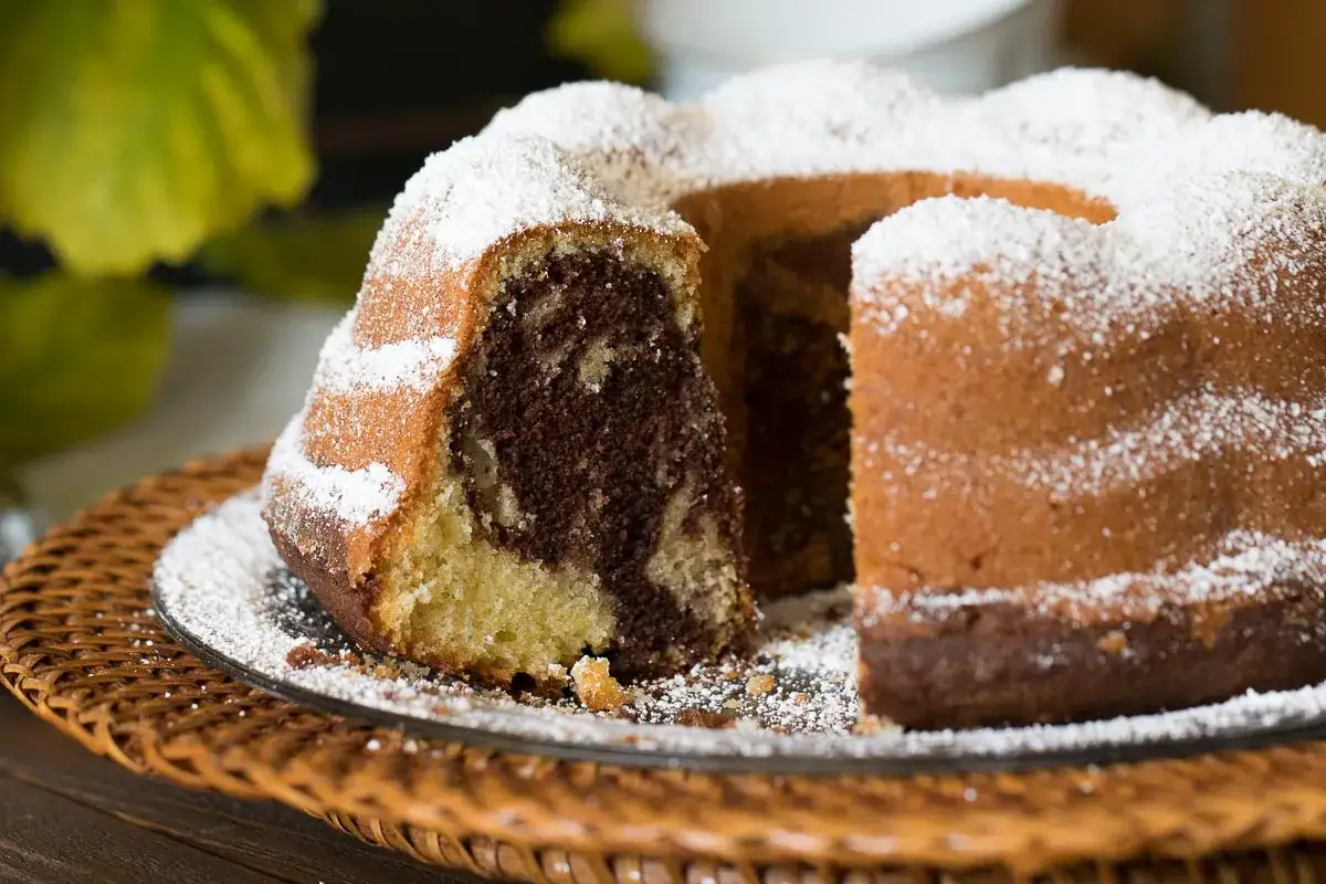 Ein saftiger Marmorkuchen, bestäubt mit Puderzucker, wartet darauf, nach diesem einfachen Marmorkuchen Rezept gebacken zu werden.