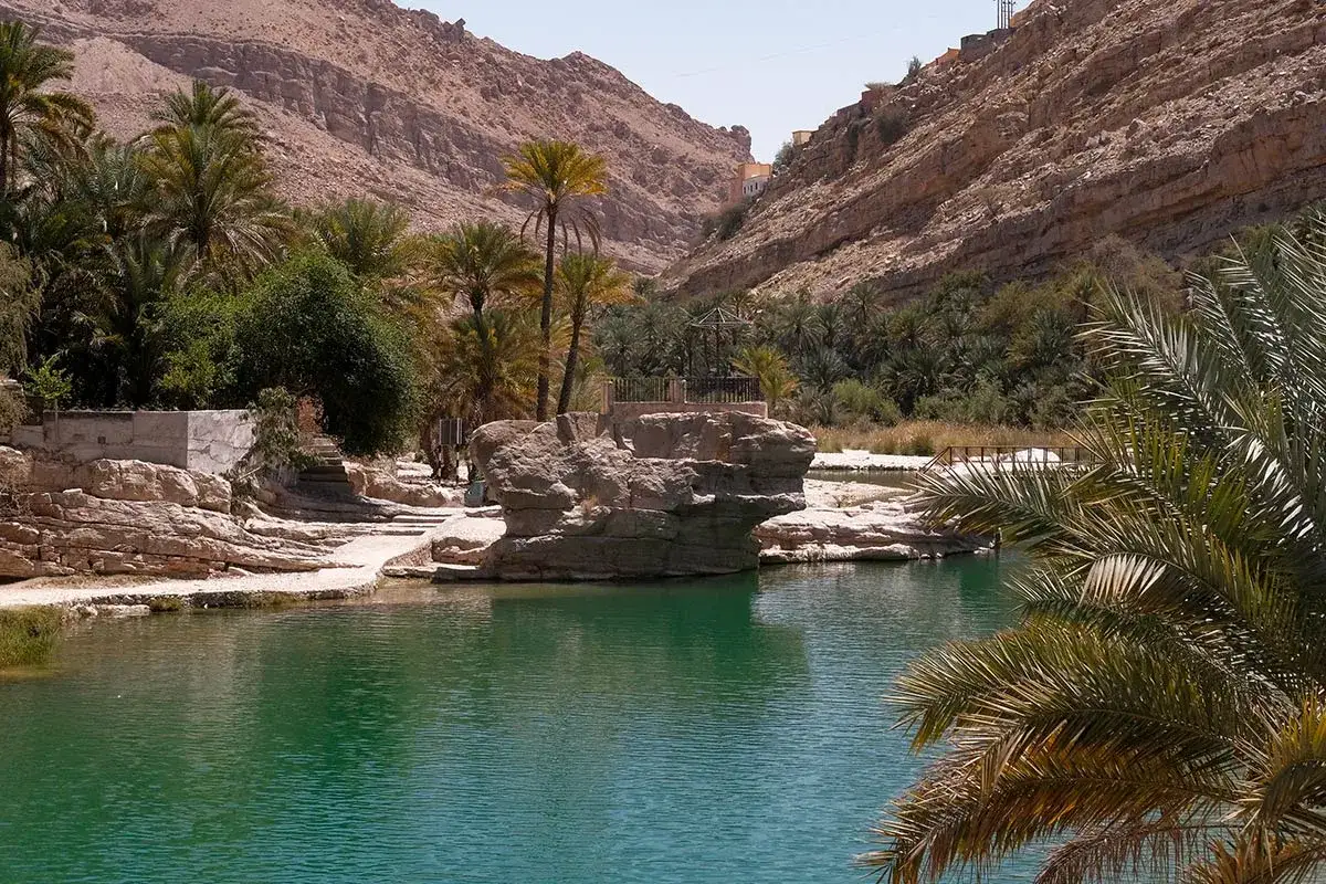 Oase in Oman mit türkisfarbenem Wasser, Palmen und Felsen. Ein toller Tipp für Oman Reisetipps!