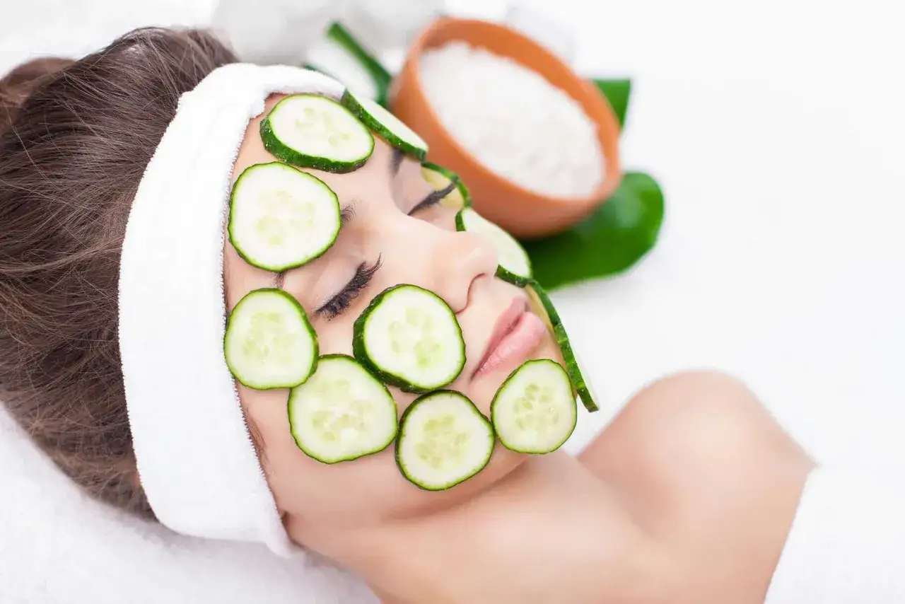 Une femme au visage couvert de rondelles de concombre, une astuce beauté pour savoir s'il faut éplucher un concombre pour un soin.
