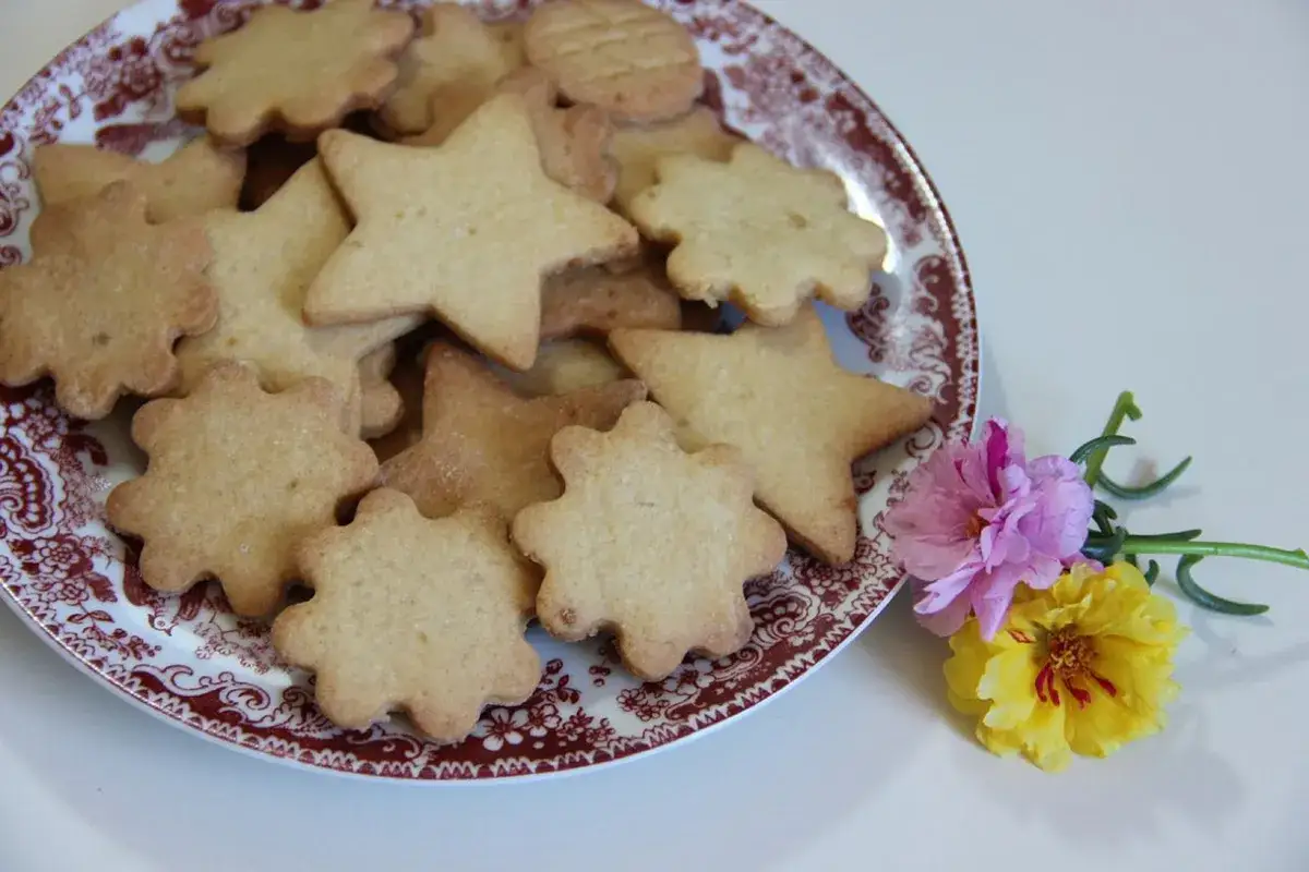 Piatto di biscotti con farina di riso senza uova, a forma di stelle e fiori, decorato con due piccoli fiori colorati.