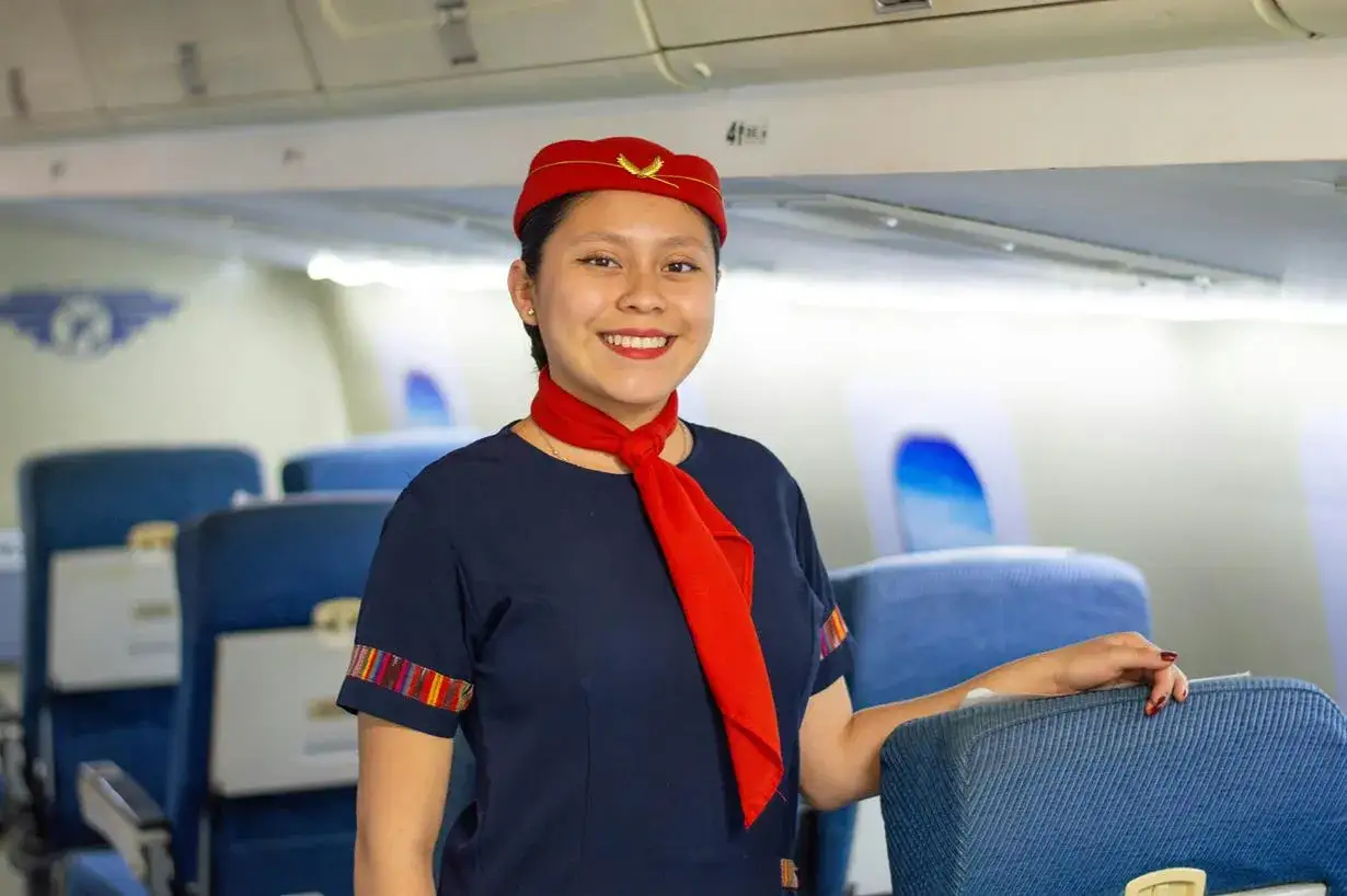 Uśmiechnięta stewardessa w czerwonym beretku i z szalikiem, gotowa do lotu. Marzysz, jak zostać stewardessą? To zdjęcie może być Twoją inspiracją!