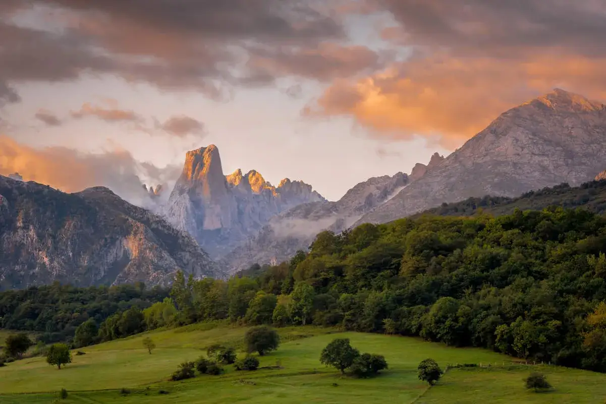 Majestuosas monta&ntilde;as iluminadas por el atardecer, un prado verde y frondosos bosques, un paisaje id&iacute;lico de los parques de Espa&ntilde;a.