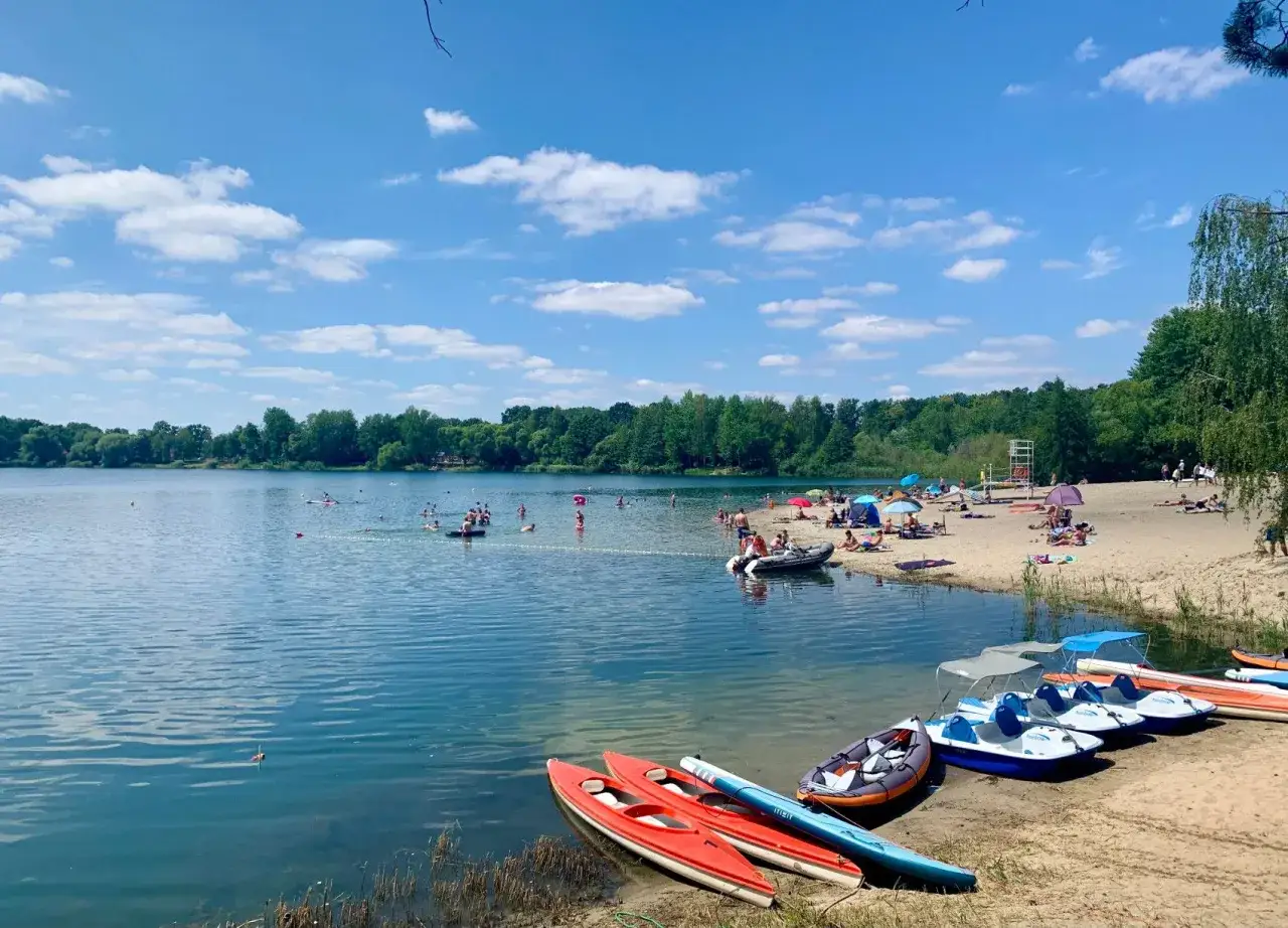 Słoneczny dzień nad jeziorem Głębocko Opolskie. Ludzie kąpią się, opalają na plaży i pływają kajakami oraz rowerami wodnymi.