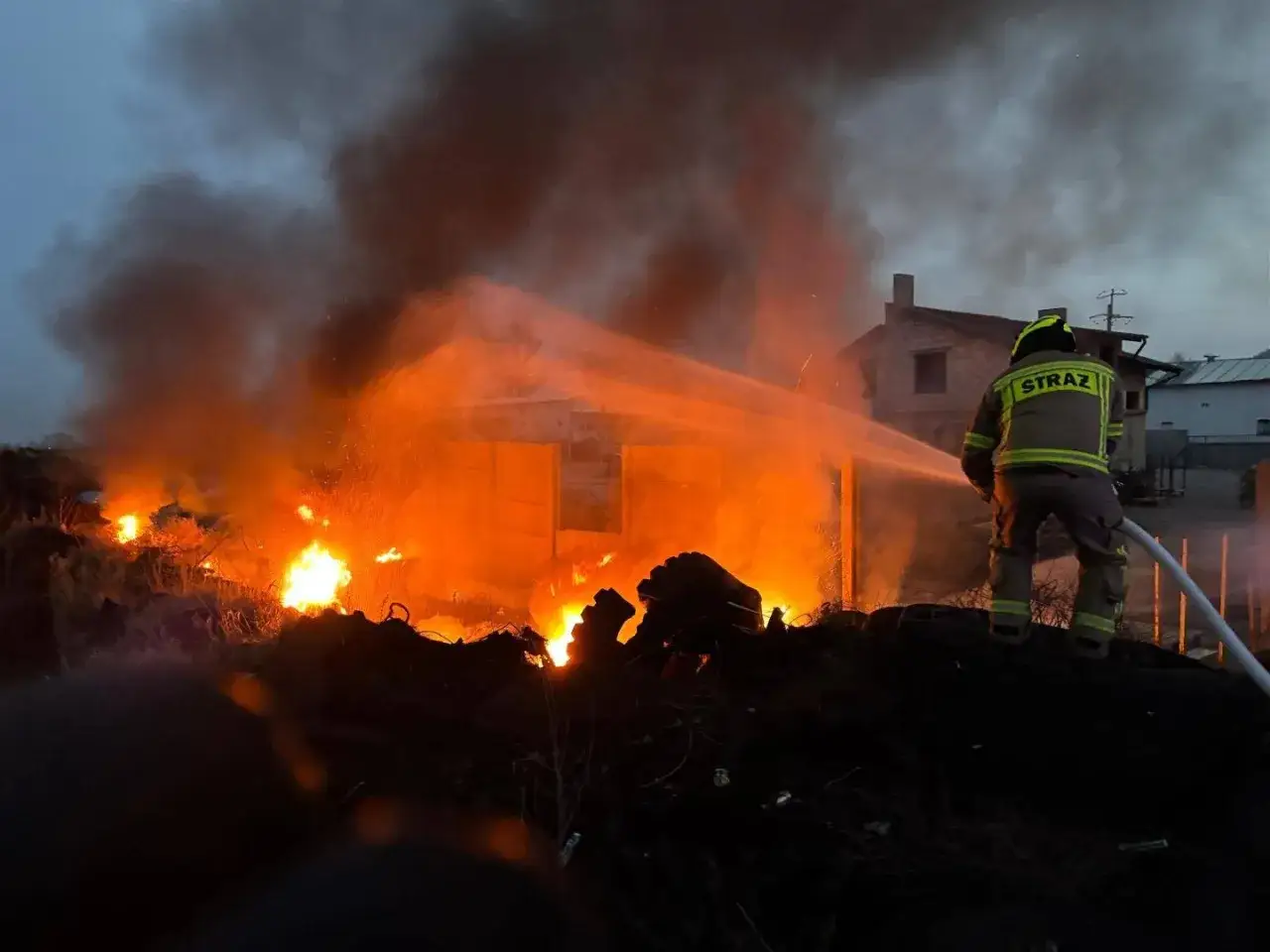 Strażak walczy z pożarem składowiska opon, z kt&oacute;rego wydobywa się gęsty dym i płomienie.