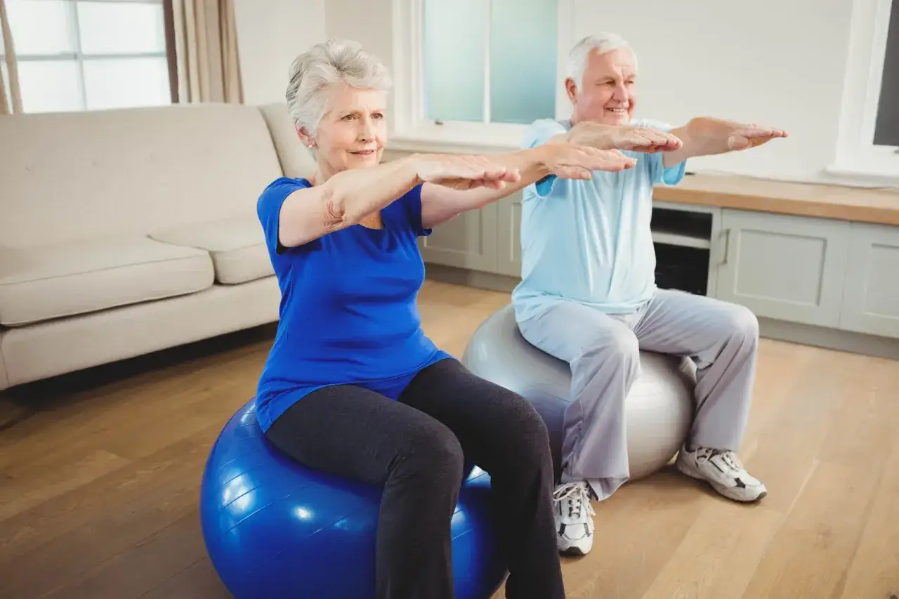 Para ćwiczy gimnastykę dla seniorów 60 plus na piłkach fitness.