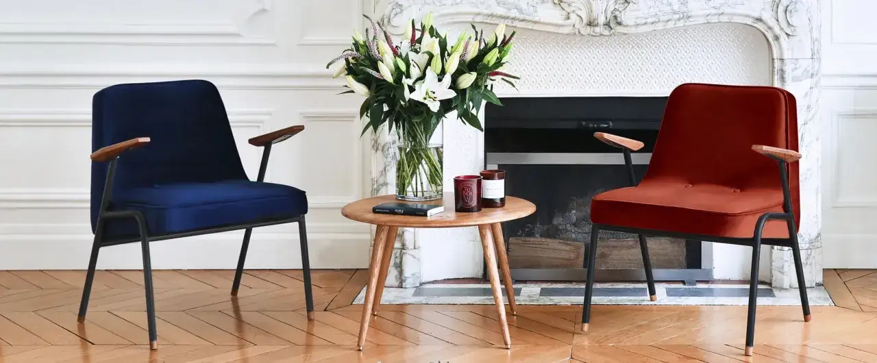 Dwa fotele w stylu mid century modern, granatowy i rudy, przy okrągłym stoliku z bukietem lilii.