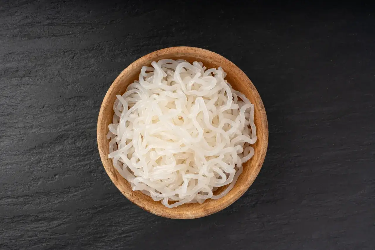 Makaron konjac co to? Białe, przezroczyste nitki w drewnianej miseczce na ciemnym tle.