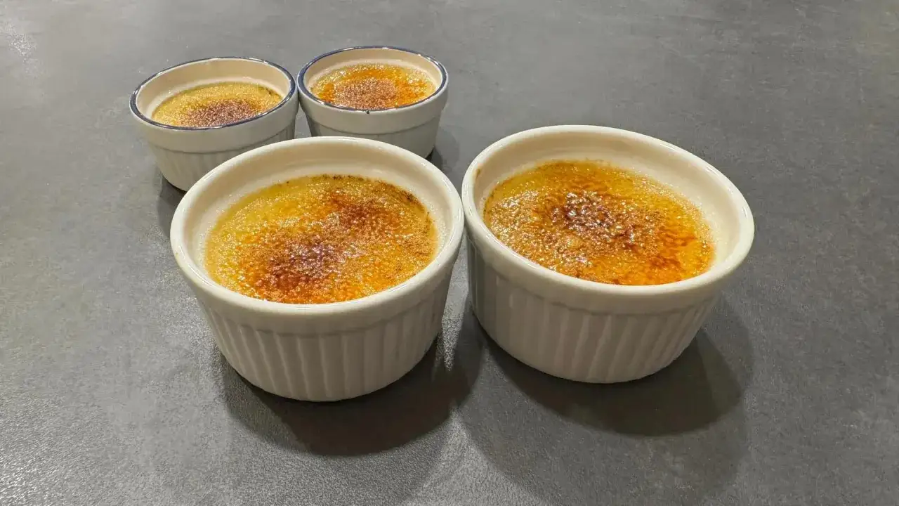 Fyra små vita skålar med gyllene, karamelliserad yta. En perfekt creme brulee redo att avnjutas.