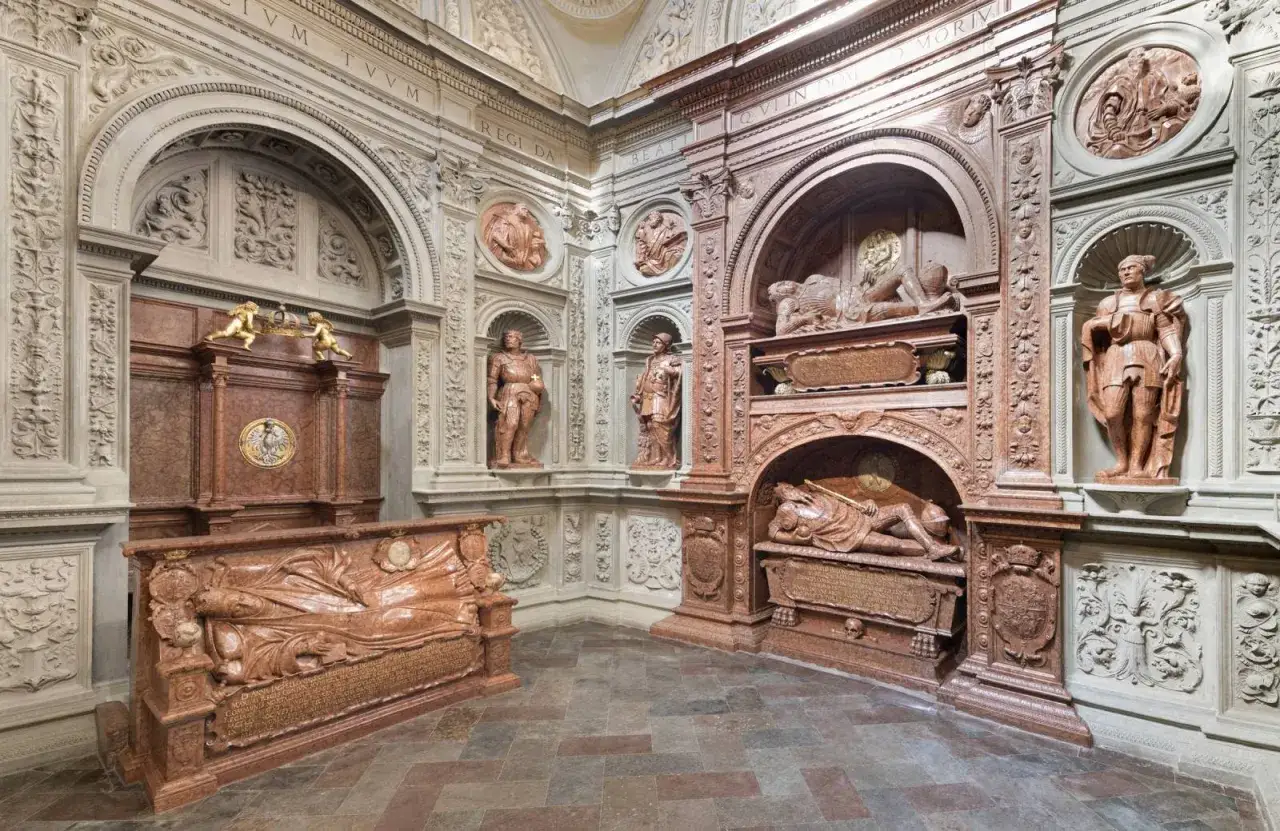 Wawel krypty: marmurowe nagrobki z rzeźbami postaci i detalami architektonicznymi, tworzące monumentalną przestrzeń grobową.