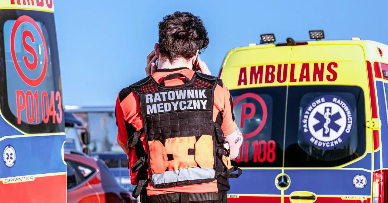 Ratownik medyczny w kamizelce rozmawia przez telefon obok ambulansu. Chcesz wiedzieć, jak zostać ratownikiem medycznym?