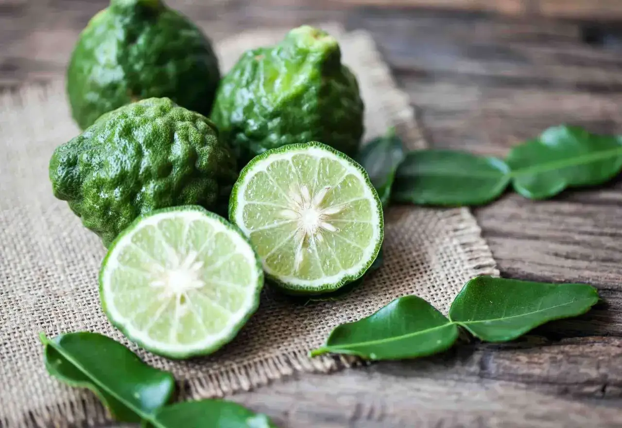Bergamotas verdes, una cortada por la mitad, sobre tela de arpillera y madera. El aroma cítrico de la bergamota que es.