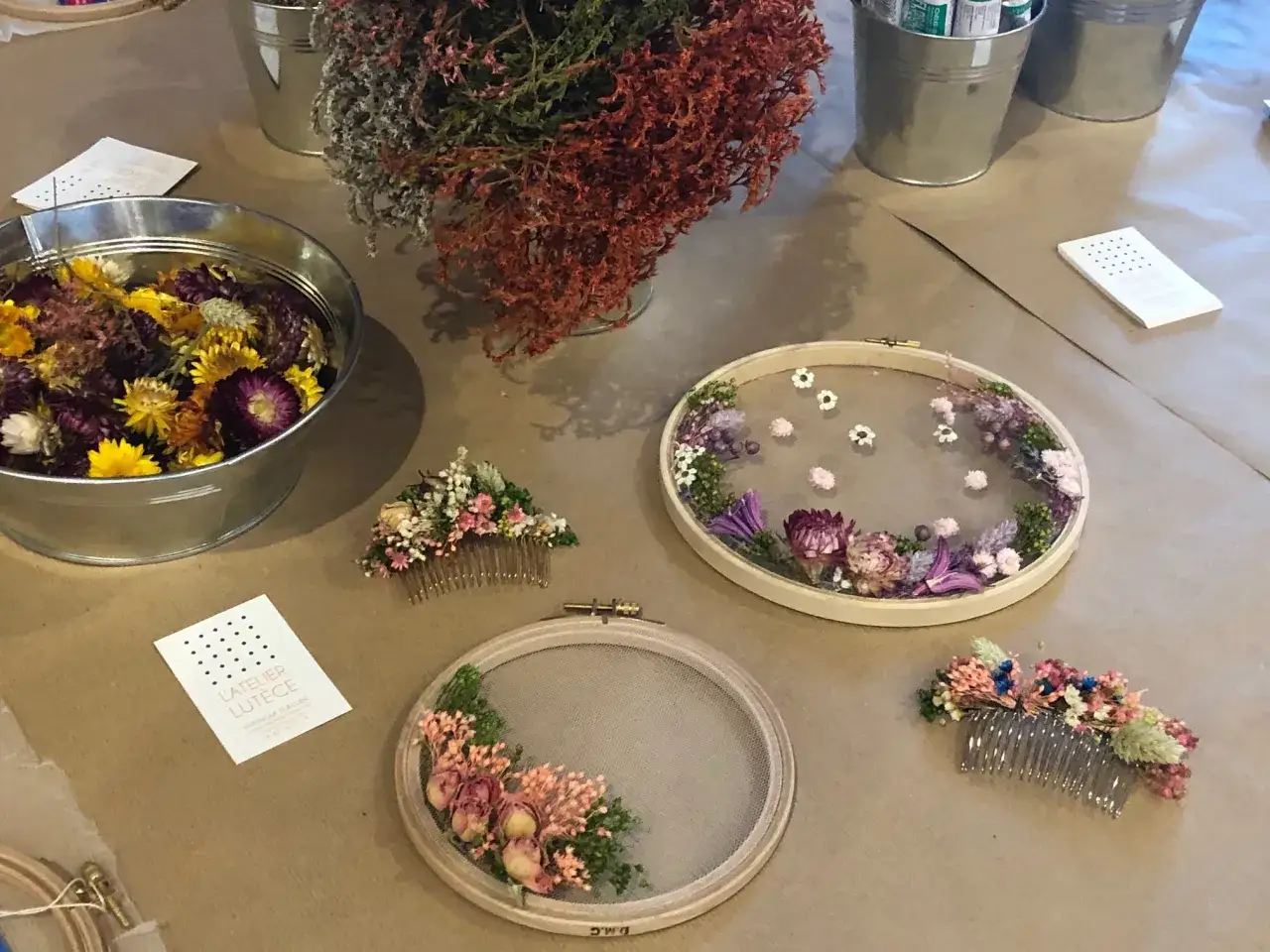 Atelier fleurs séchées : créations délicates en cours sur des tambours à broder et peignes ornés de fleurs séchées.