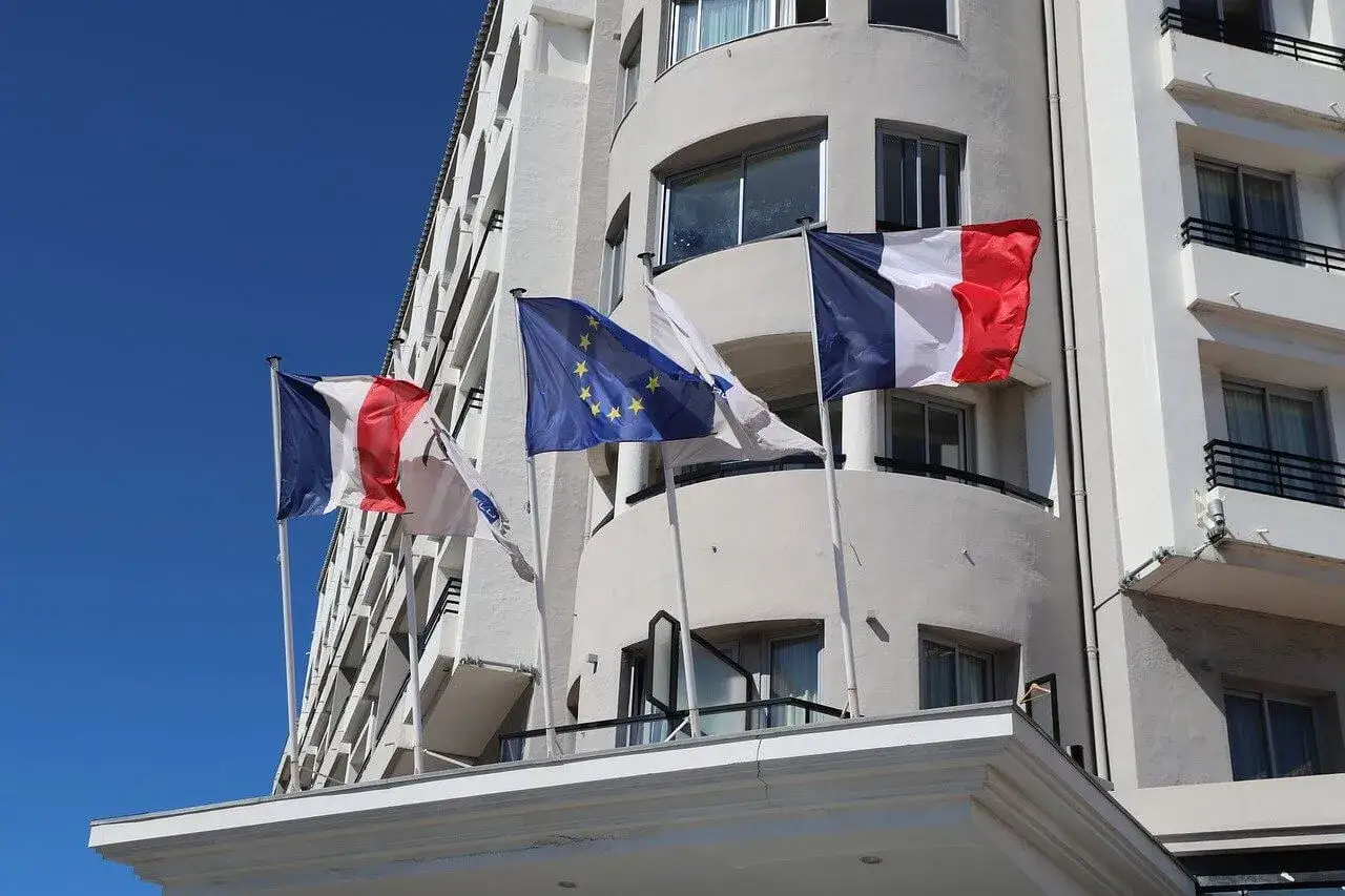 Drapeaux fran&ccedil;ais et europ&eacute;en flottant devant un b&acirc;timent blanc, symbole d'un projet de r&eacute;novation &eacute;nerg&eacute;tique.