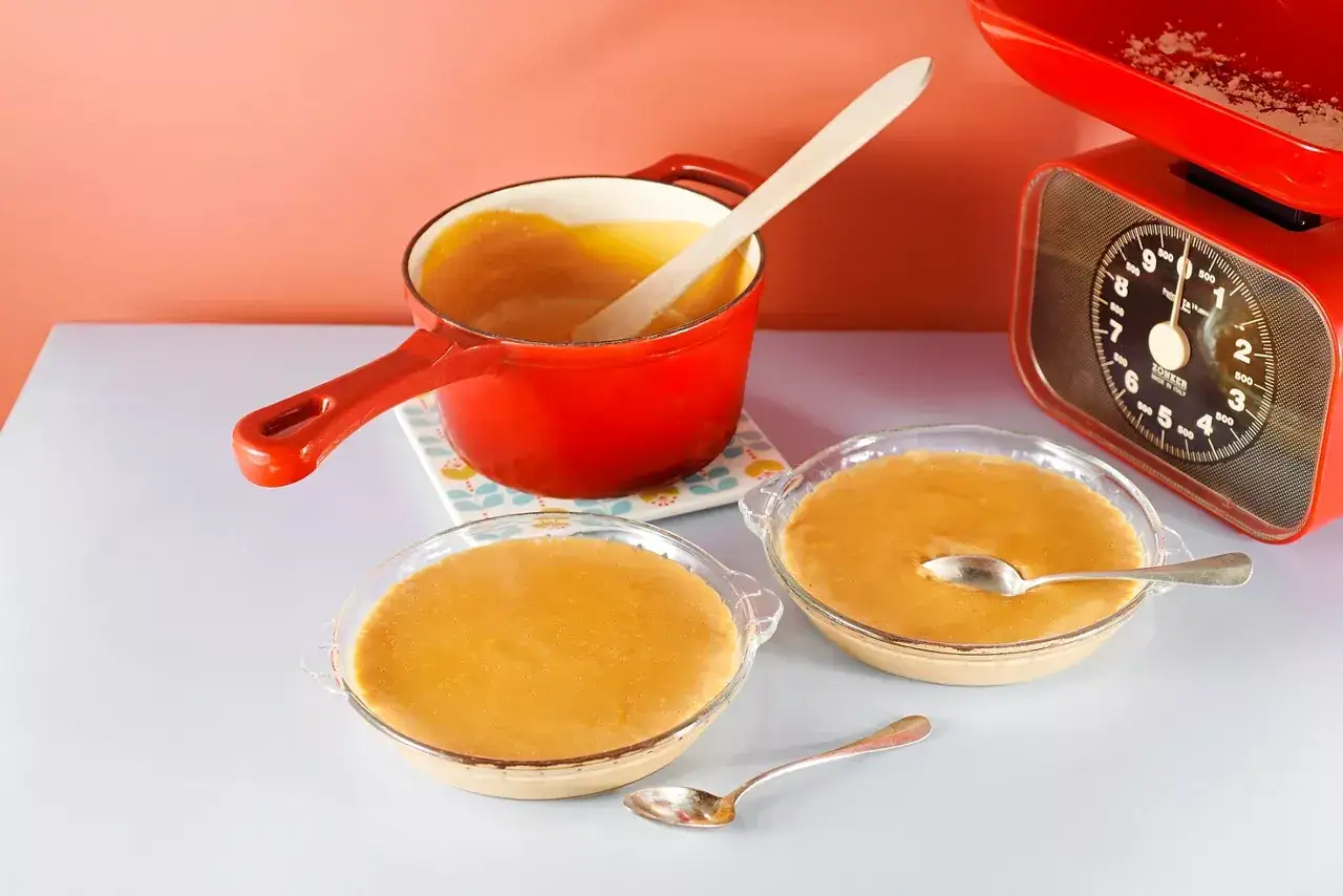 Deux bols de crème dessert onctueuse, prêts à être dégustés. Une casserole rouge contient du caramel liquide, attendant d'être versé.