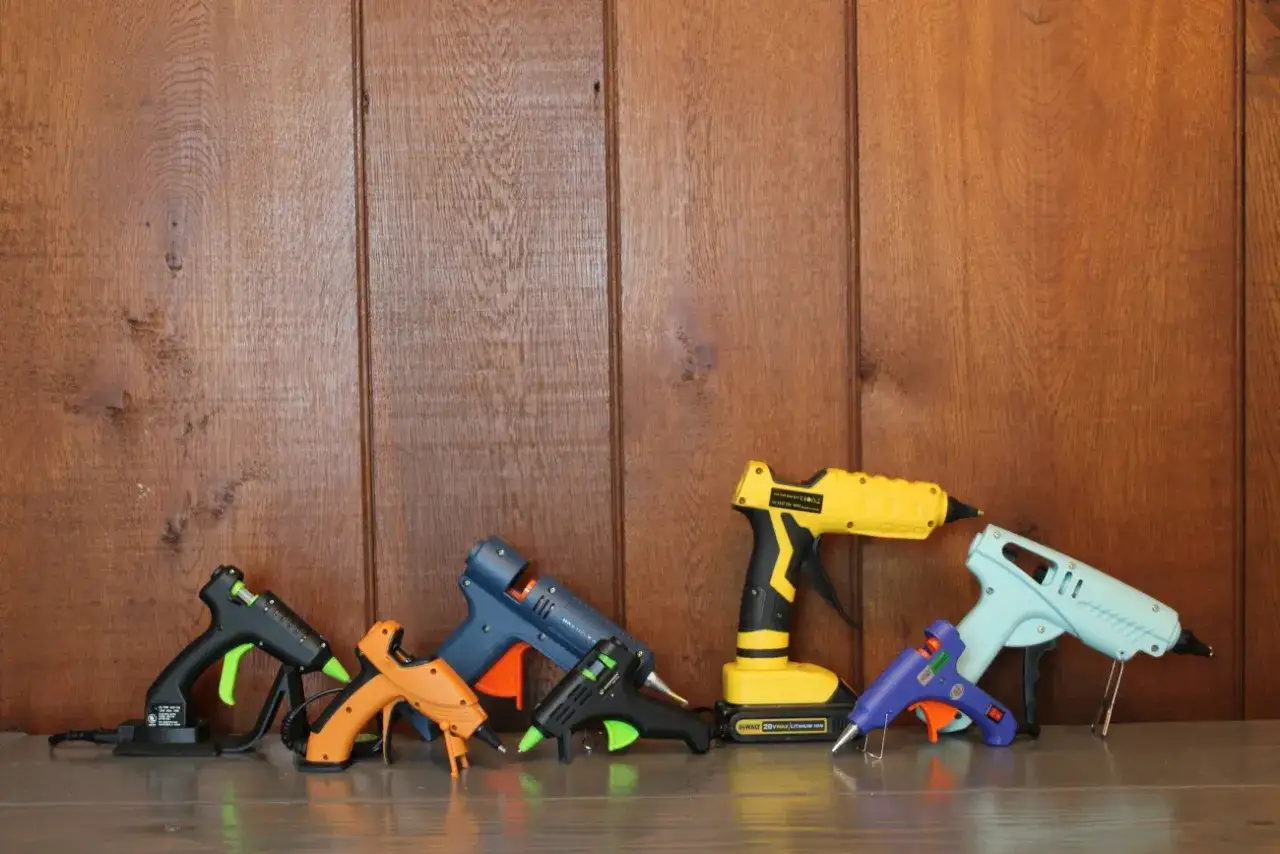 A collection of colorful hot glue guns, from small to large, lined up against a wooden background. Will hot glue hold up outside?