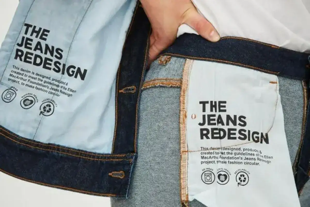 Detalle de etiqueta interior de vaqueros que promueve una **marca sostenible** y la moda circular, con iconos de reutilización y reciclaje.
