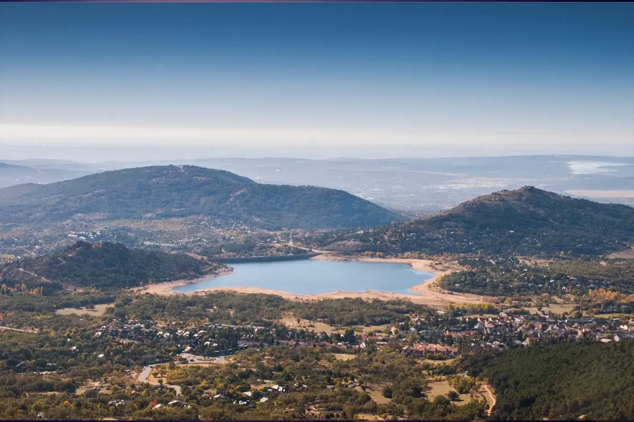 Vista panorámica de un embalse rodeado de montañas y pueblos, ideal para explorar los mercadillos de la sierra de Madrid.