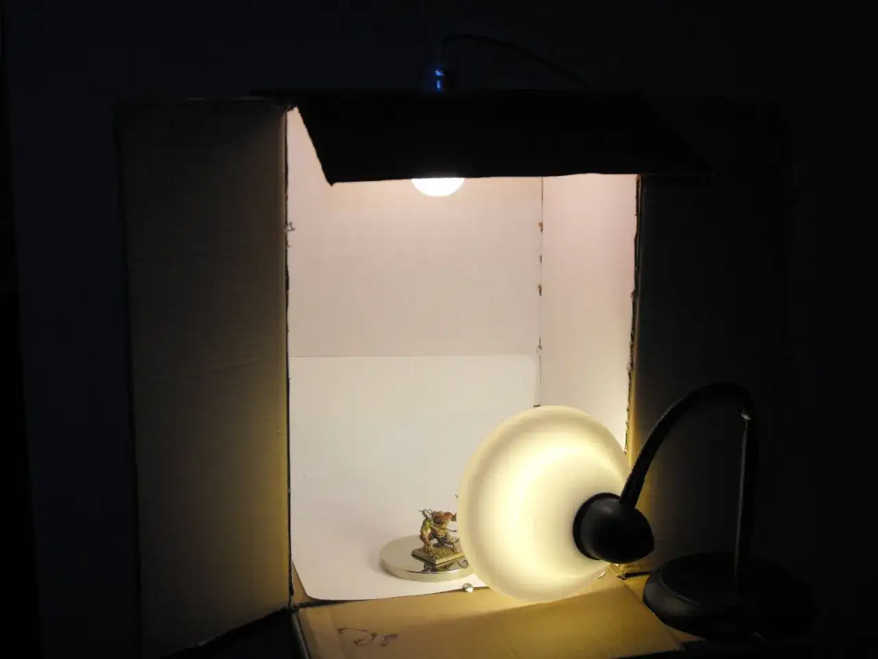Domowa makrofotografia: mała figurka w kartonowym namiocie świetlnym, oświetlona lampką.