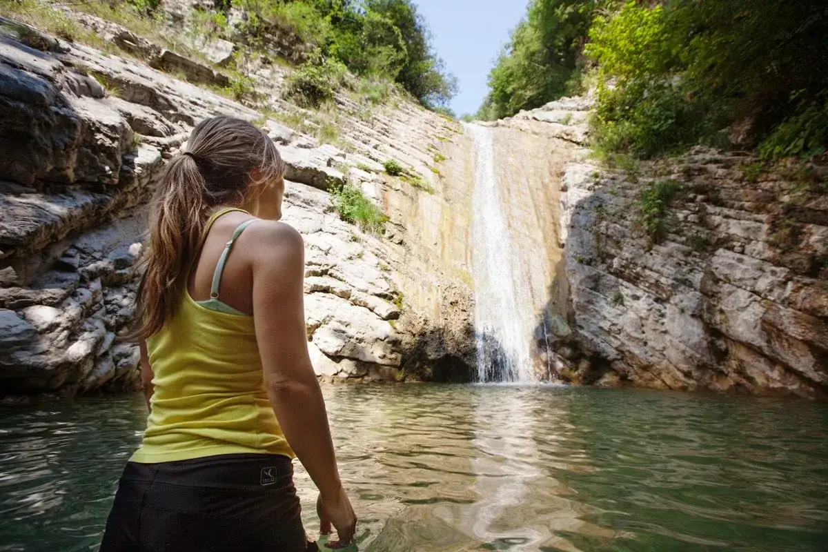Ragazza ammira le cascate di Tignale, immersa in un ruscello cristallino tra rocce e vegetazione rigogliosa.
