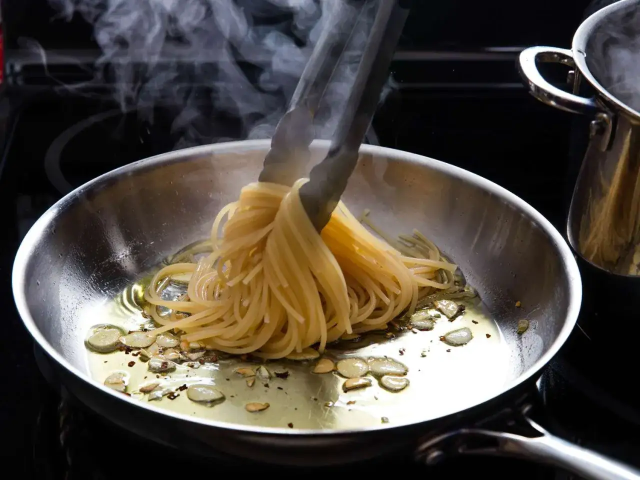 Dampfender Spaghetti-Bund wird in einer Pfanne mit Oliven&ouml;l und Knoblauch f&uuml;r ein authentisches Spaghetti Aioli Original geschwenkt.