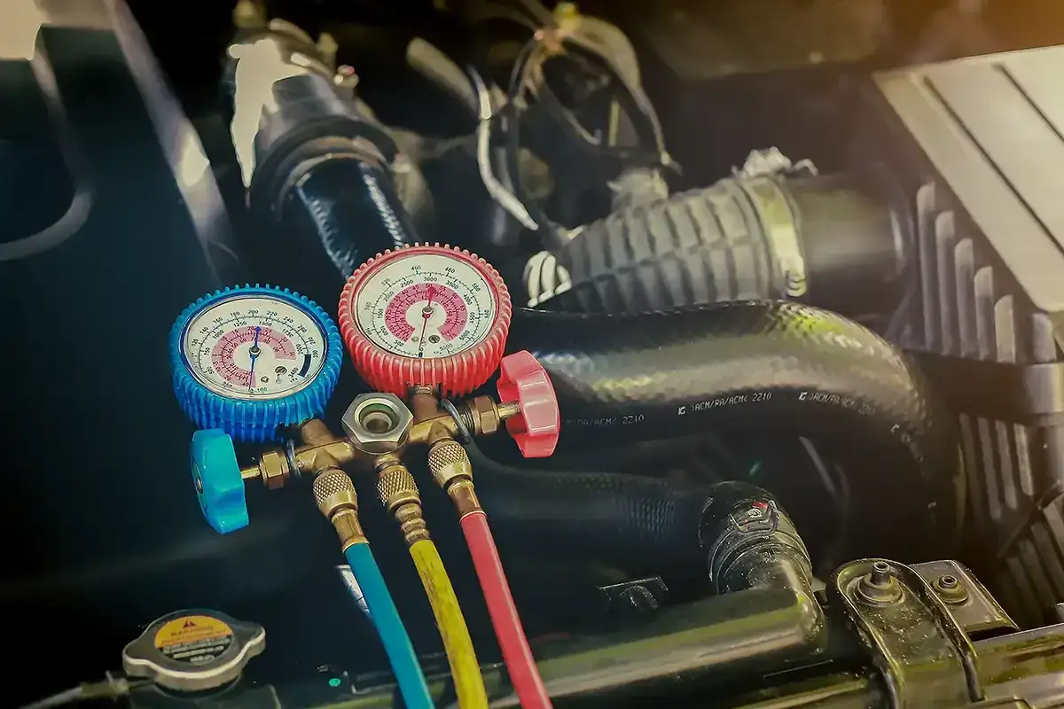 Car AC manifold gauges connected to engine hoses, suggesting a car thermostat replacement or AC service.