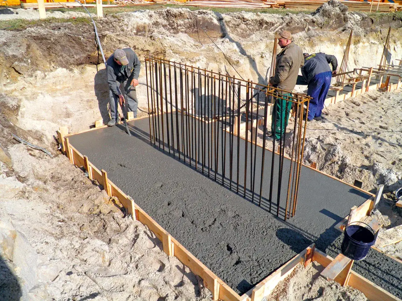 Budowa fundamentów: pracownicy wylewają beton, przygotowując strop. Zbrojenie czeka na zalanie.