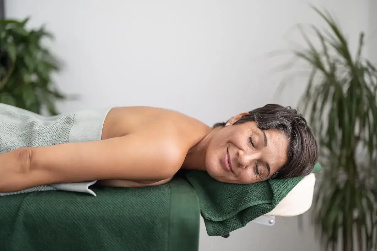En kvinna vilar p&aring; en massageb&auml;nk, med slutna &ouml;gon och ett fridfullt leende. En ny b&ouml;rjan, livet efter utmattningssyndrom.
