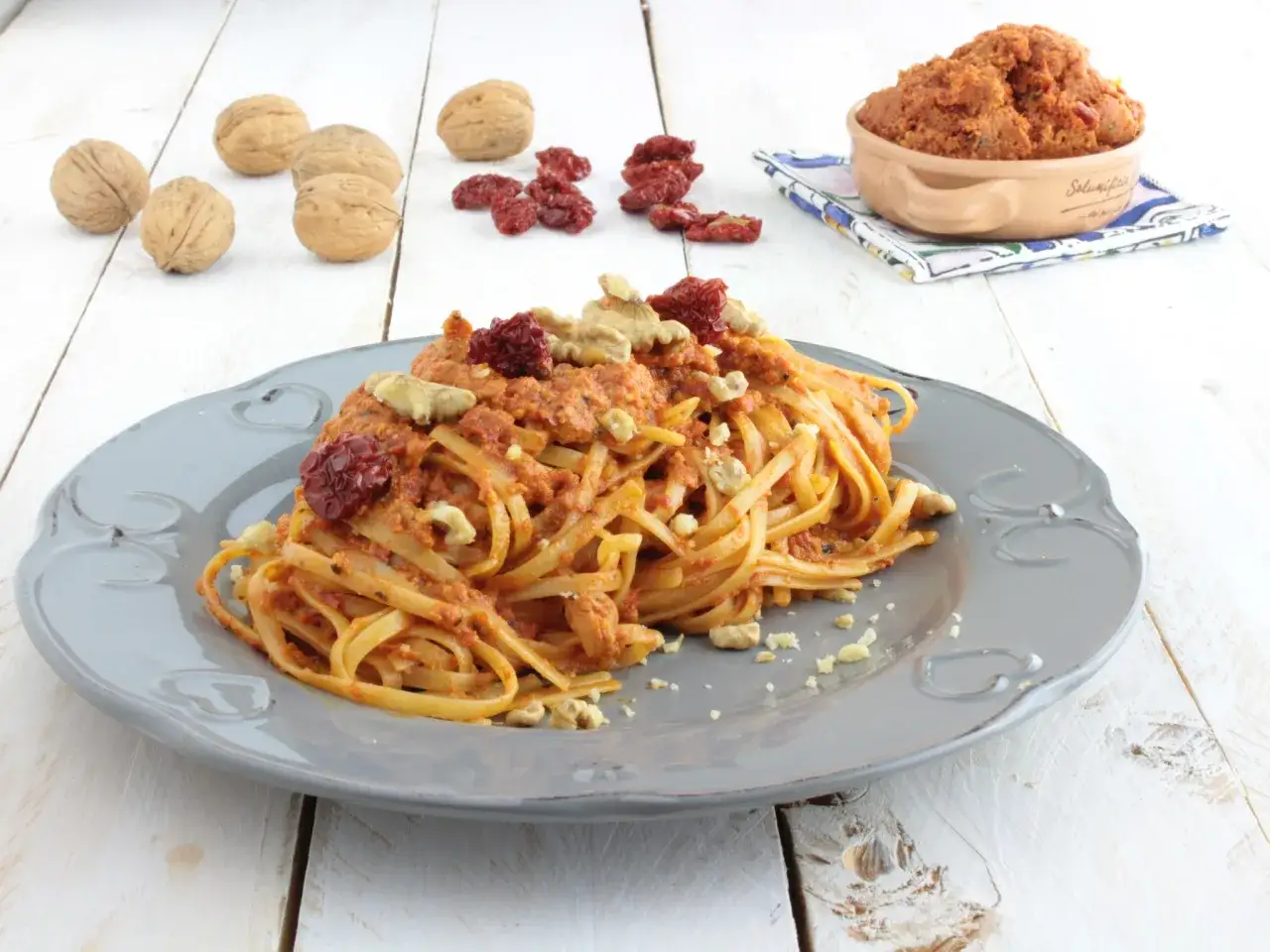 Linguine condite con pesto di pomodori secchi e noci, guarnite con noci intere e pomodorini secchi.