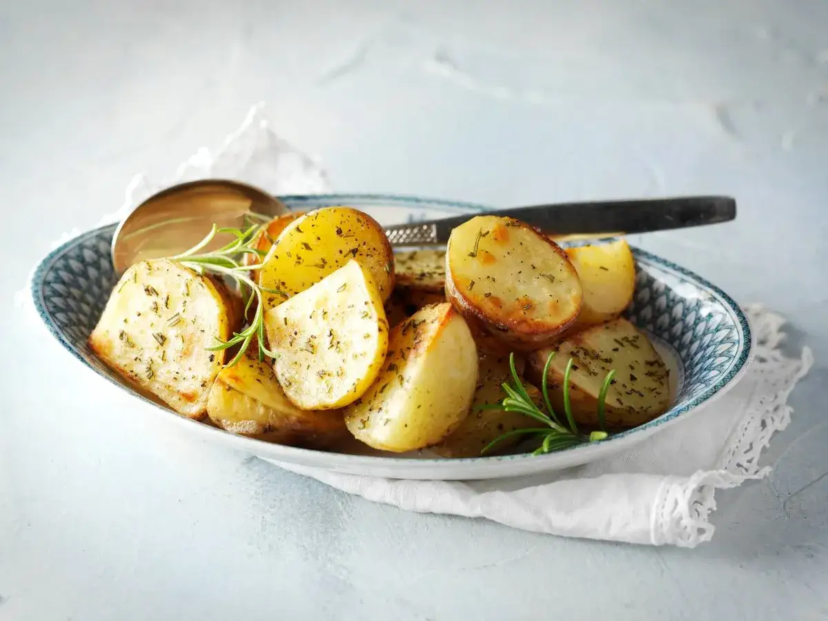 En sk&aring;l med gyllene, kryddade confiterad potatis, garnerad med rosmarin. En sked ligger i sk&aring;len.