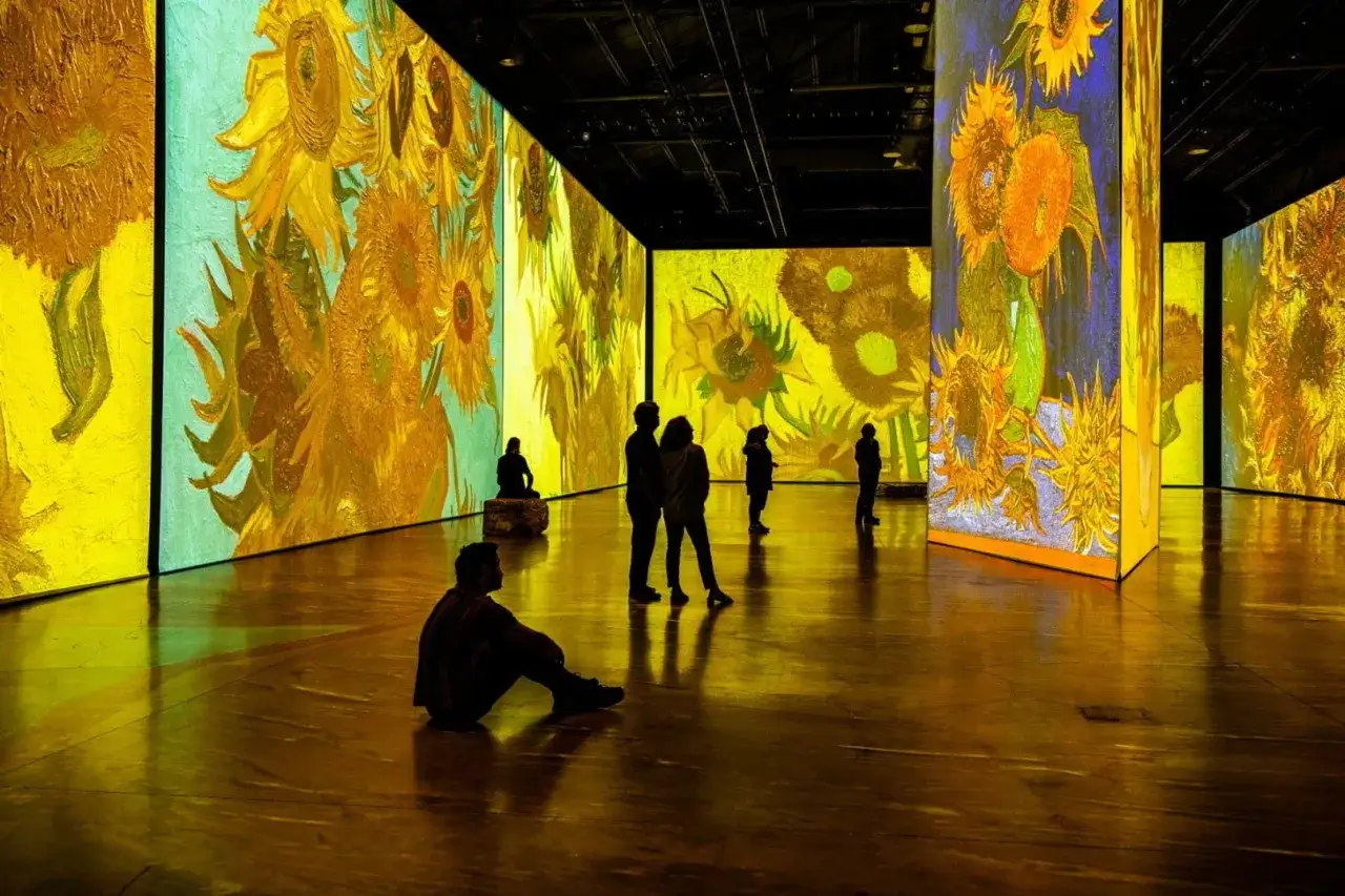 En uppslukande utställning där Van Goghs solrosor projiceras på väggar och golv, vilket ger en känsla av att van gogh alive. Besökare sitter och står och beundrar konstverken.