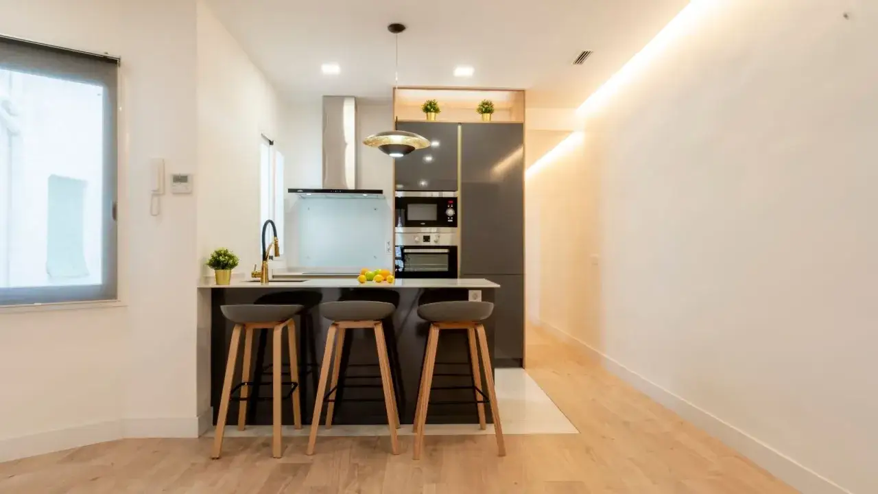 Cocina moderna con isla y taburetes, ideal para ideas cocinas peque&ntilde;as. Electrodom&eacute;sticos integrados y grifer&iacute;a dorada.