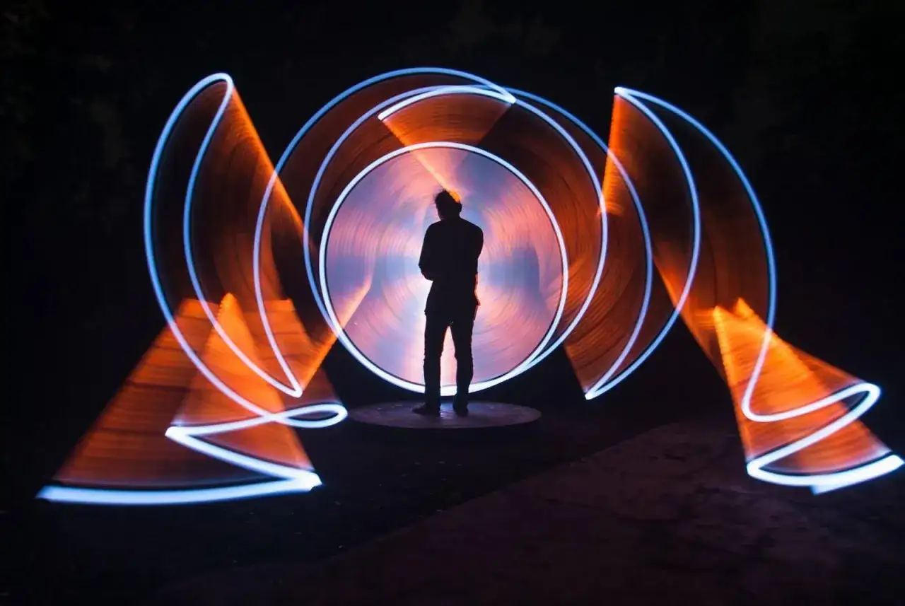 Silhouette di uomo al centro di un vortice di luce arancione e blu, un esempio di light painting fotografia.