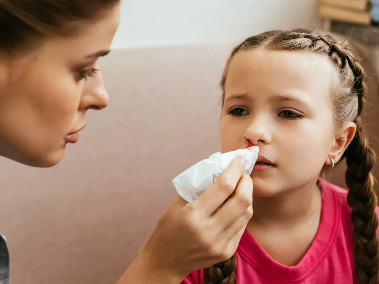 Mama delikatnie przemywa dziecku krew z nosa u dziecka z jednej dziurki chusteczką.