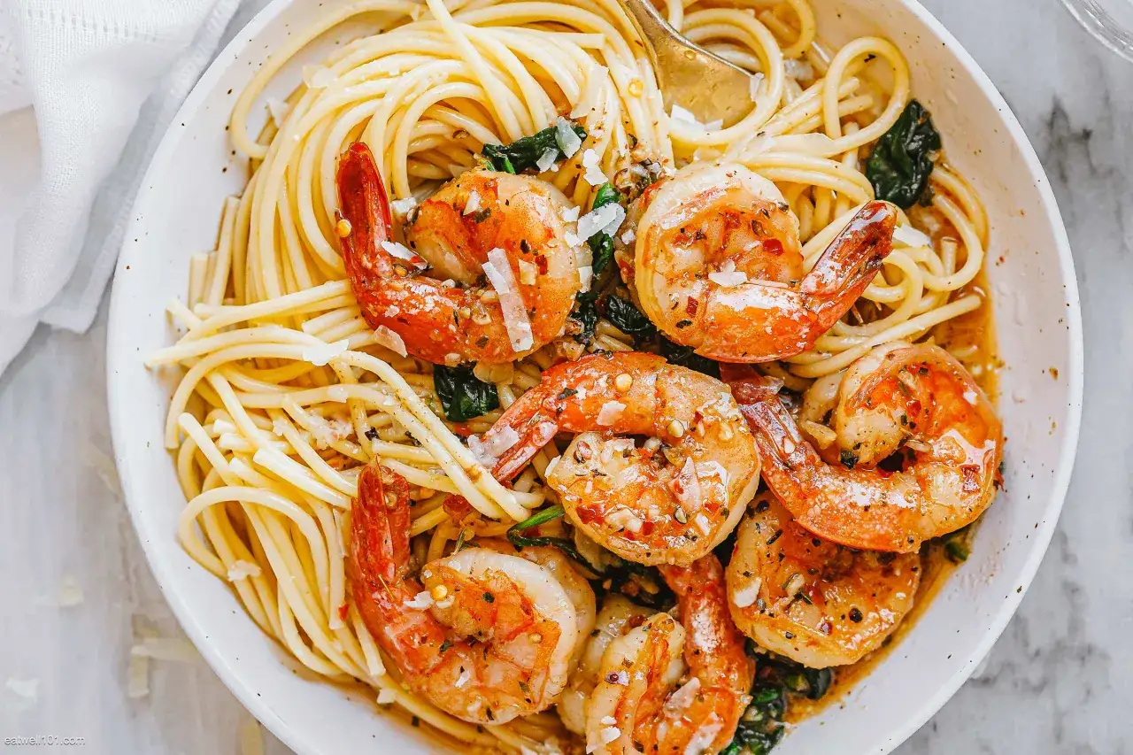 Teller mit Spaghetti mit Garnelen, garniert mit Parmesan und Kräutern. Ein goldener Löffel ragt aus der köstlichen Mahlzeit.