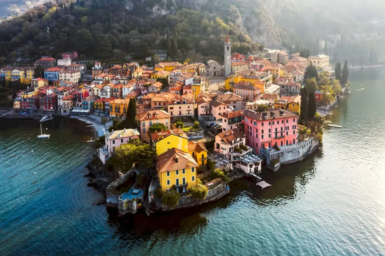 F&auml;rgstark by vid en sj&ouml;, ett av m&aring;nga mysiga resm&aring;l i Italien. En kyrka med torn reser sig &ouml;ver de pastellf&auml;rgade husen.