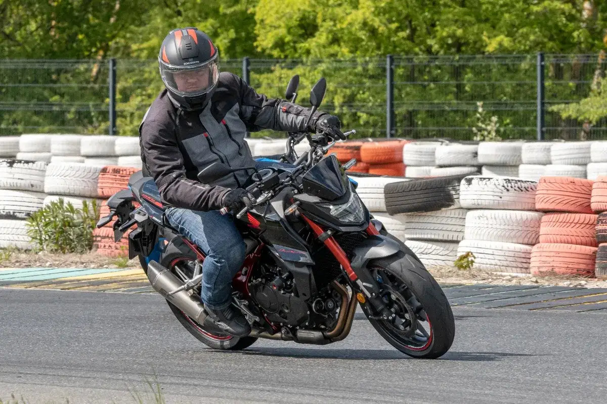 Motocyklista w kasku i kurtce jedzie na czarnym motocyklu Honda Hornet 750 po torze wyścigowym, otoczonym oponami.