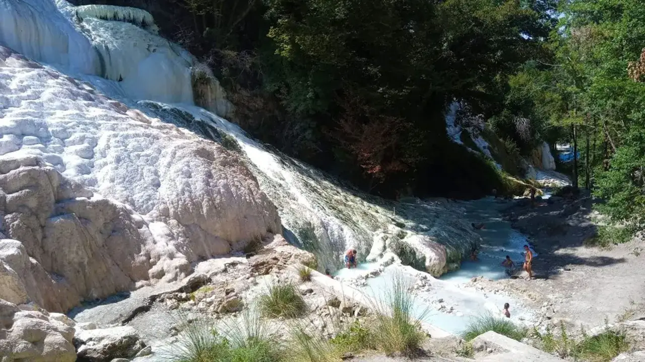 Cascades d'eau thermale aux formations calcaires blanches &agrave; San Casciano dei Bagni, o&ugrave; des baigneurs profitent de l'eau bleue turquoise.