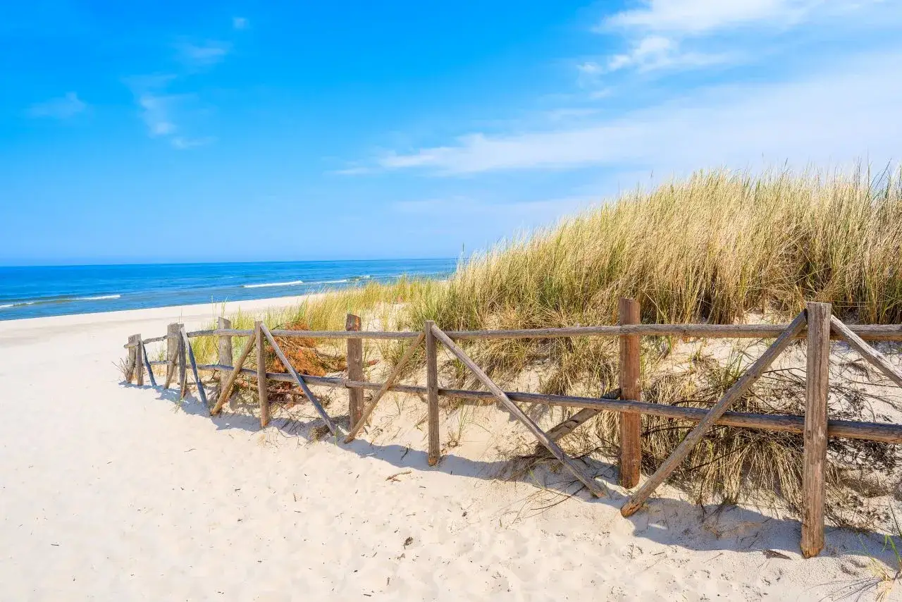 Piękne wydmy lubiatowskie z drewnianym płotkiem prowadzącym na piaszczystą plażę i błękitne morze.