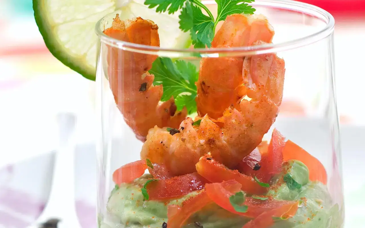 Verrine langoustine : crevettes roses sur avocat, tomates et coriandre, garnie d'une tranche de citron vert.
