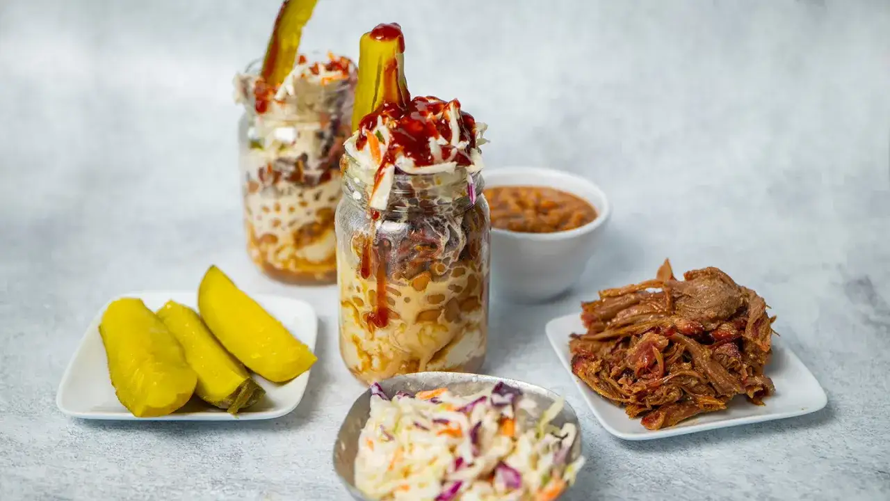 Un d&eacute;lice de pulled pork servi en pot avec salade de chou, haricots et cornichons.