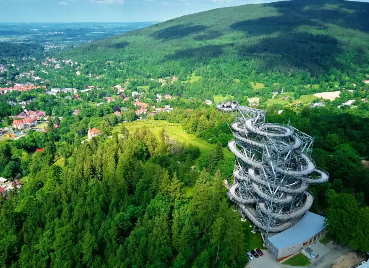 Widok na wieżę widokową w Zieleńcu, malowniczej części **Karpat Polska**. Spiralne schody wiodą na szczyt, skąd rozpościera się panorama na gęste lasy i okoliczne zabudowania.