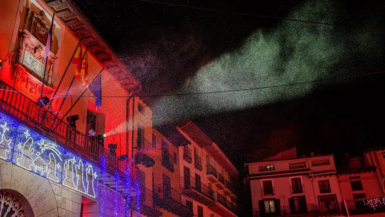 Luces y nieve artificial iluminan el mercadillo navideño de Calatayud. Edificios históricos se visten de fiesta con decoraciones festivas.
