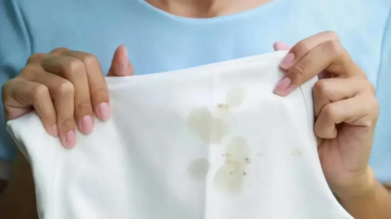 Manos sostienen tela blanca con manchas de grasa, mostrando c&oacute;mo quitar grasa de la ropa.