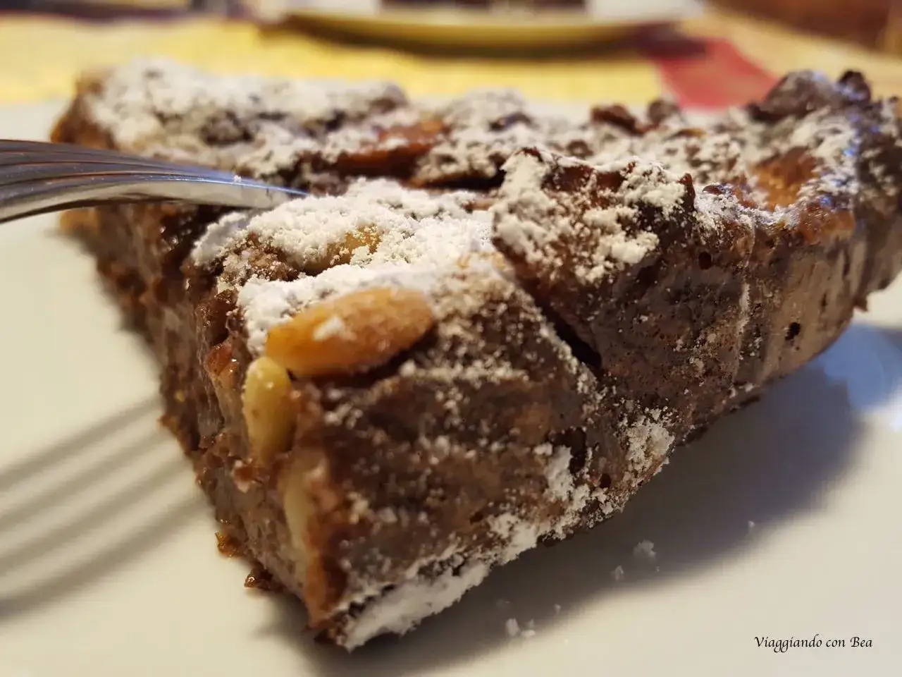 Una fetta di torta di pane ricetta della nonna, cosparsa di zucchero a velo e pinoli, pronta per essere gustata.